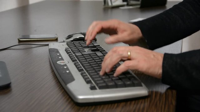 Hands of a man working at computer typing on keywords on dark desktop
