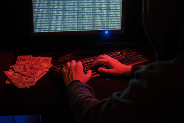 The man in the hood checks the malicious code on the keyboard. Cybercrime through the Internet.