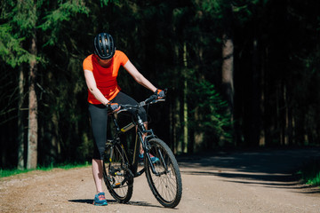 Young pretty woman in helmet and orange shirt sitting on bicycle on the forest road. Healthy lifestyle concept. Sports Girl with bike.