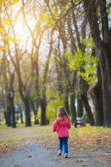 Rear view of running little girl in autumn park.Lens flare