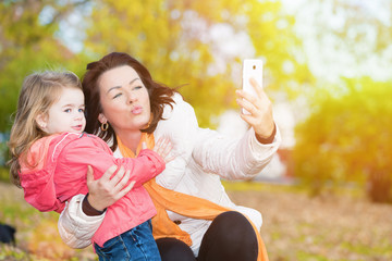 Mother and daughter taking self portrait photo , selfie, in the autumn park.Lens flare