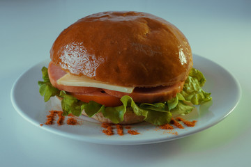 A large and tasty hamburger with sausage, cheese, tomatoes and a salad leaf on a white plate.