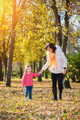 Naklejka na ściany i meble Mother and daughter walking through the autumn park.Lens flare.Focus on the daughter face