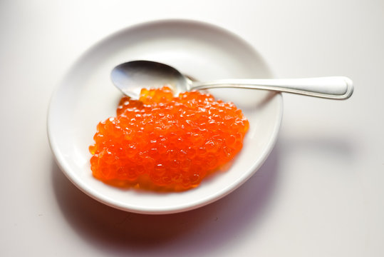 Red caviar in a white plate, closeup light background