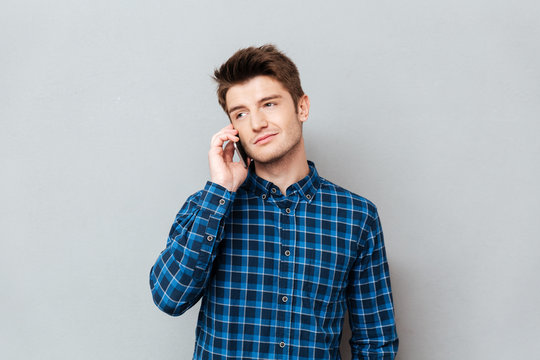Handsome man standing over grey wall and talking by phone.