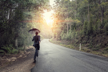 Obraz premium Back view of businessman with umbrella and suitcase walking on road