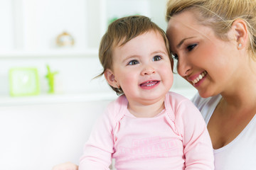 Smiling mom and baby sitting on the couch together.Baby looking away.Shallow doff