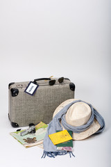 Preparing for a journey. Vintage suitcase with a map, travel documents, a hat, money and sunglasses, displayed on a white background.