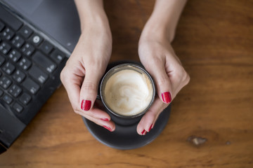 close up of woman hand holding hot coffee cup on wooden table