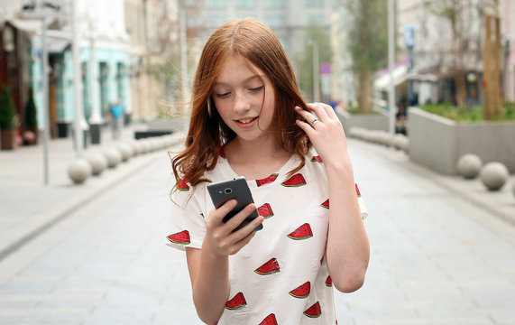 Front view of a fashion happy girl walking and using a smart phone on a city street