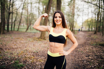 Fototapeta premium Fitness girl in park showing biceps against park background