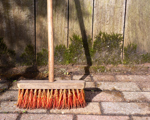 Old broom against wooden background to clean up a garden path
