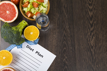 Food and sheet of paper with a diet plan on a dark wooden table.