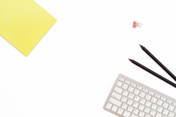 yellow Notepad, computer keyboard, two black pencil and a clip for paper on white background. Minimal working concept office Desk.