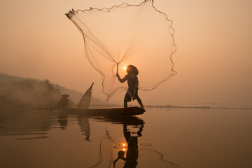 Fisherman catching fish at dawn in Thailand