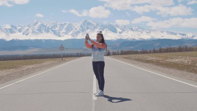 Alone woman tourist is taking pictures on smart phone while tay on the road highway with mountains on background