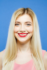 Studio Shot of Pretty Female Face with Perfect Skin and Professional Makeup. Closeup Portrait of Blond-haired Young Woman with Wonderful Smile on Blue Background.