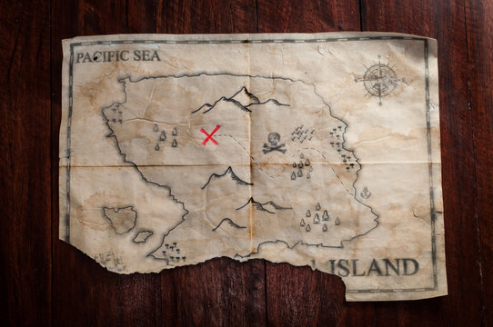 Top view to vintage fake crumpled treasure map on wooden table. Fake pirate handmade map with red cross as place of Treasure chest