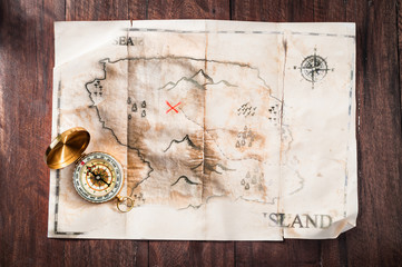 Fake vintage old broken map on wooden desk with compass. Pirates treasure map