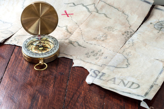 Nautical compass in front of fake pirates treasure map on wooden table