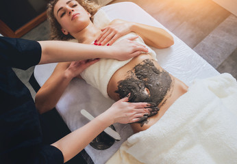Beautiful woman in spa salon getting mud body massage
