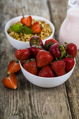 Muesli, smoothies, milk and fresh strawberries on a wooden table.