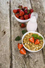 Muesli, smoothies, milk and fresh strawberries on a wooden table.