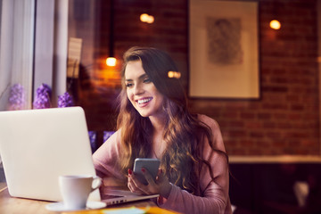 Happy woman using laptop and smartphone at cafe