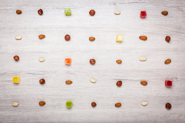 nuts, almonds, hazelnuts and jelly candies on a light wooden surface lined with symmetrical rows. Beautiful background of candy and nuts.