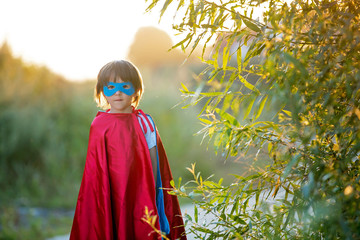 Cute sweet little preschool child, boy, playing superhero on a rural path in a small village