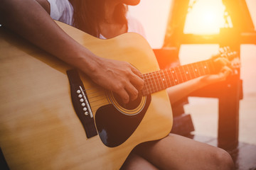 Young woman playing guitar while sitting on the beach.