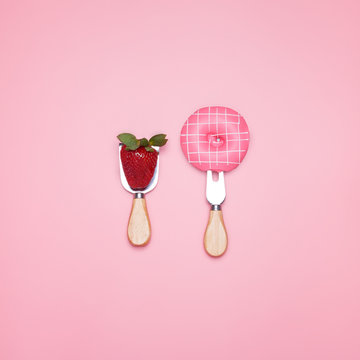 Top view of a pink donut on a fork and fresh ripe strawberry on a pastel pink background. Minimal design.
