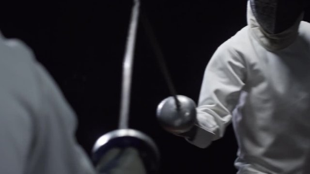 Slow motion studio shot of two fencers in protective masks and costumes fighting with foils