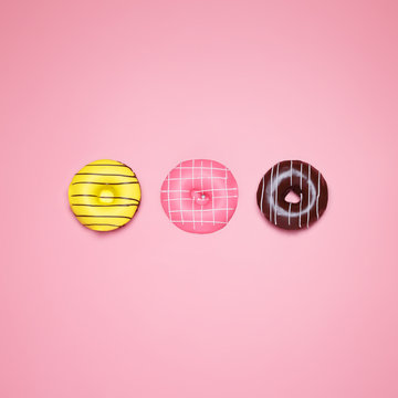 Top view of a Banana, strawberry and chocolate donuts on a pastel pink background. Minimal concept junk food