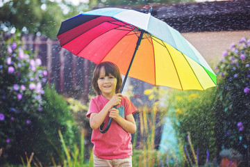 Cute adorable child, boy, playing with colorful umbrella under sprinkling water