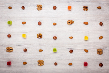 nuts, almonds, hazelnuts and jelly candies on a light wooden surface lined with symmetrical rows. Beautiful background of candy and nuts.