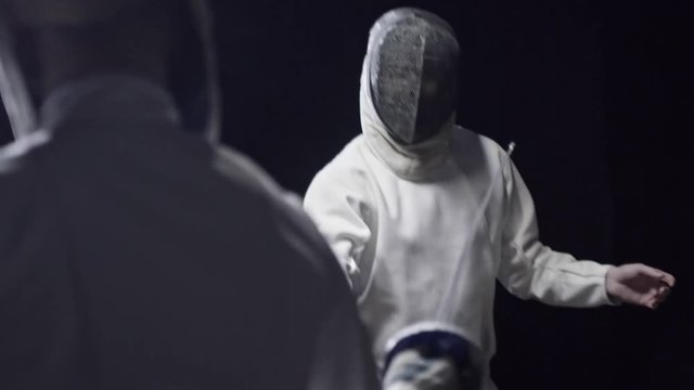 Two opponents in protective masks and costumes practicing fencing fight. Slow motion shot