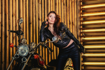 Fototapeta na wymiar Beautiful biker woman in leather jacket,standing next to his motorcycle . The spirit of freedom and independence.