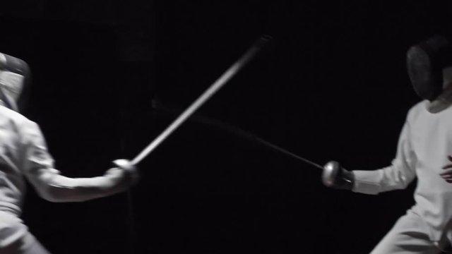 Slow motion of two fencers competing in foil fighting in dark studio