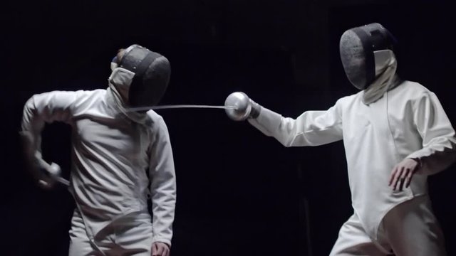 Slow motion of fencer in protective uniform hitting his opponent with foil while scoring at sword fight