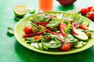 Fresh spring salad with arugula, spinach, beet leaves, tomatoes, cucumber slices and sweet pepper on green wooden table. Selective focus