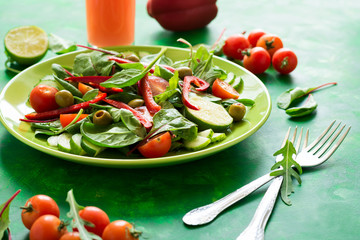 Fresh spring salad with arugula, spinach, beet leaves, tomatoes, cucumber slices and sweet pepper on green wooden table. Selective focus