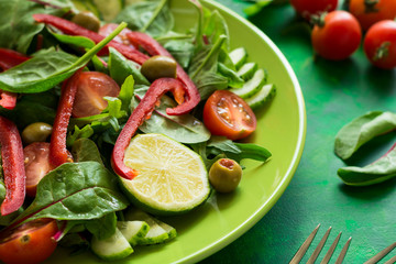 Fresh spring salad with arugula, spinach, beet leaves, tomatoes, cucumber slices and sweet pepper on green wooden table. Selective focus