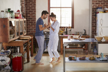 Hispanic couple in pyjamas dancing in kitchen, full length