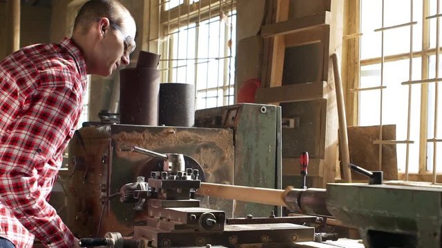 Caucasian male in goggles and red plaid shirt operating turning machine in joinery. Footage in slowmotion