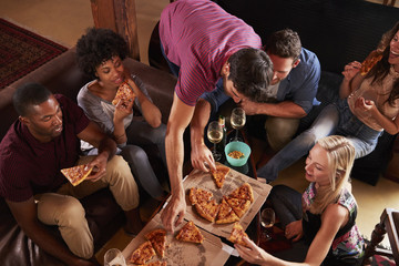 Young adults eating pizzas at a party at home, elevated view