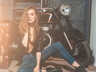 Fototapeta na wymiar Pretty biker girl standing with vintage suitcase at motorcycle