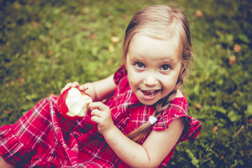 Cute little girl with apples in a green grass.