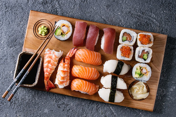Sushi Set nigiri and sushi rolls on wooden serving board with soy sauce and chopsticks over black stone texture background. Top view with space. Japan menu