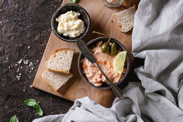 Black bowl of salmon pate with red caviar served with butter, sliced bread, capers, vintage knife...